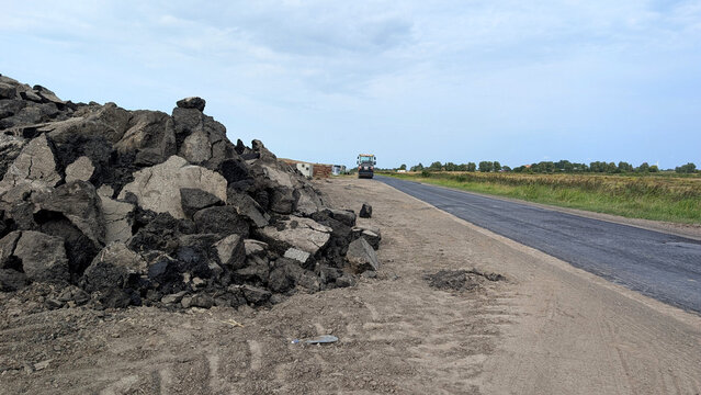 Road construction with fresh asphalt pavement and pile of broken asphalt. 