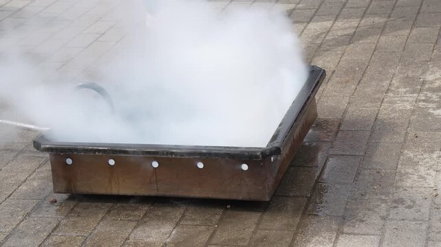 Intense fire burning inside a metal training pan with bright orange flames during a safety drill on a paved outdoor surface
