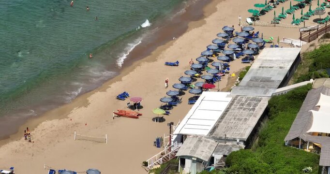 Aerial view of a sandy beach with green and blue umbrellas in rows, beach club building, people swimming and sunbathing, turquoise sea, summer vacation in Italy on the Mediterranean coast