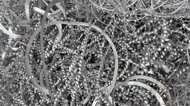 Pushing into a tangled heap of aluminium turnings waste from an industrial lathe or CNC machine engineering scrap for recycling