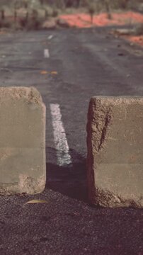 A concrete block sits on a worn road surface. The surroundings show signs of wear. Some debris and leaves are scattered nearby as daylight falls on the scene.