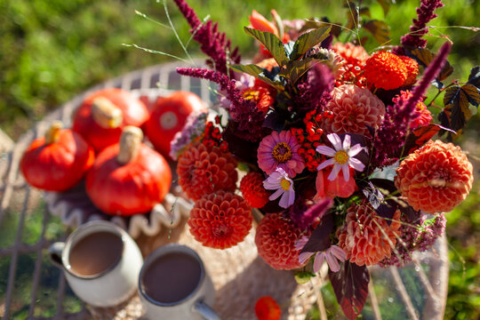 Close up of autumnal flower arrangement with orange pumpkins and coffee served in backyard. Bouquet of fall dahlias. Top view. 