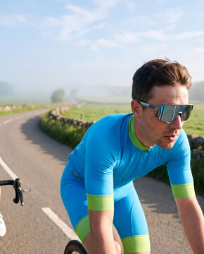 Cyclist in sport sunglasses riding a misty country road at dawn