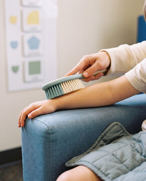 Therapist brushing a child forearm with a sensory brush in a clinic