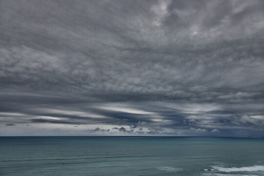 storm clouds roll over San Lorenzo Island as seen from the cliffs of Miraflores, Lima, casting a moody, atmospheric veil over the Pacific coastline. The dense cloud formations and shifting light hint 