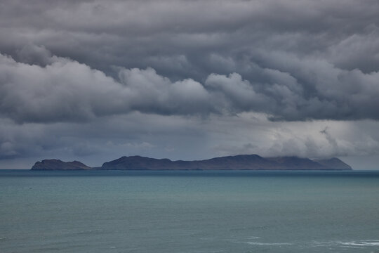 storm clouds roll over San Lorenzo Island as seen from the cliffs of Miraflores, Lima, casting a moody, atmospheric veil over the Pacific coastline. The dense cloud formations and shifting light hint 