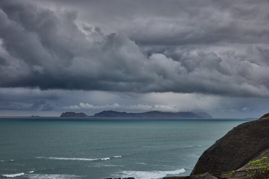 storm clouds roll over San Lorenzo Island as seen from the cliffs of Miraflores, Lima, casting a moody, atmospheric veil over the Pacific coastline. The dense cloud formations and shifting light hint 