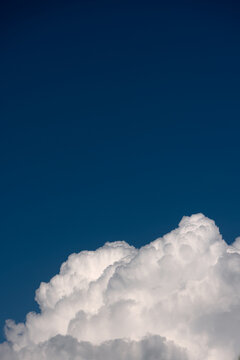 Clear blue sky background with dense white cumulus cloud formation along the bottom. Vertical minimalist cloudscape with generous copy space, crisp lighting, sunny atmosphere, and summer day.