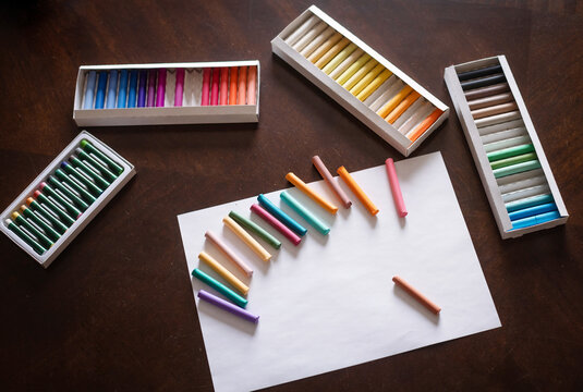 Box of soft pastel crayons and colored pencils on creative wooden table, close up