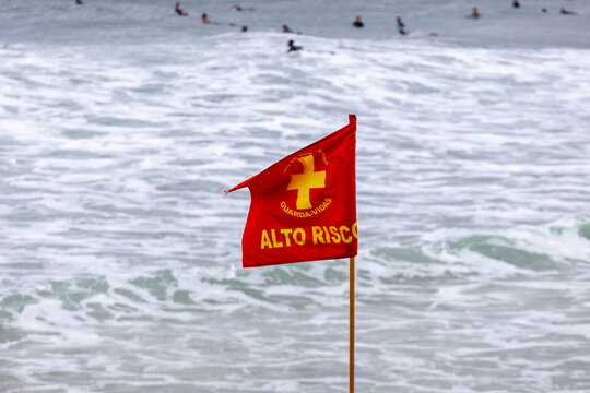 Red Lifeguard High Risk Warning Flag on a Beach with Rough Ocean Waves and Surfers