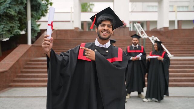 Happy indian student proudly pointing to his diploma on graduation day