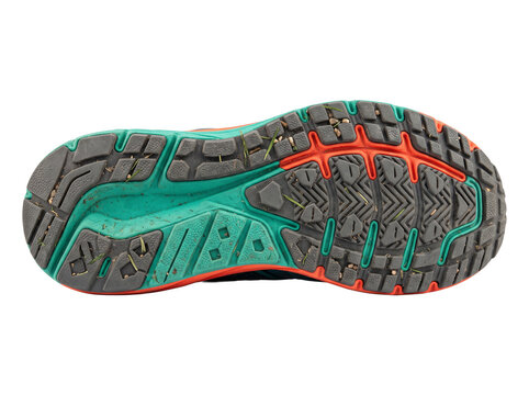 Running shoe sole dirty tread showing trail active wear close up on black background with stuck grass and pebbles, ideal for fitness, athletic training, outdoor adventure, and sports footwear gear.