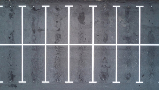 Empty parking lot with white painted lines on dark asphalt surface viewed from a high angle drone aerial perspective shot