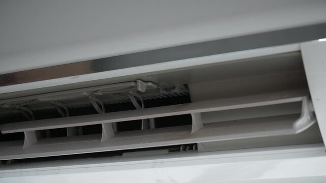 Air conditioner vent and indoor cooling system.
A close-up view shows the open air outlet and adjustable louvers of a wall-mounted split air conditioner with visible dust and internal components.