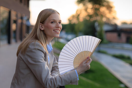 Young woman uses a fan to cool down during a heatwave while outdoors on a sunny day