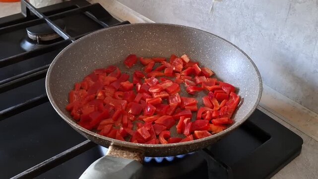 Cooking red peppers in a kitchen with oil in a frying pan on a stove