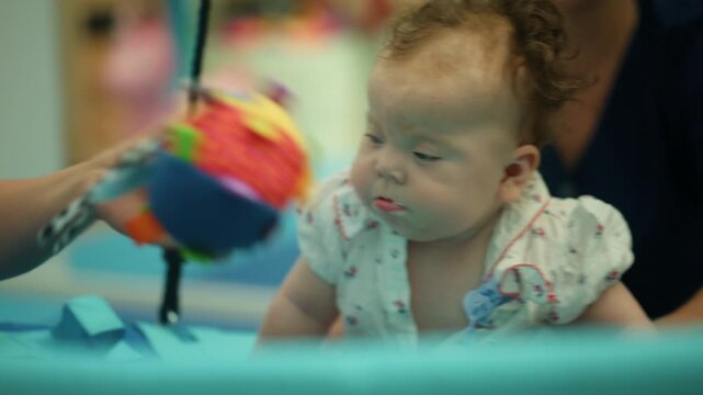 Infant girl engaging with a brightly colored developmental toy, stimulating sensory learning and physical therapy activities