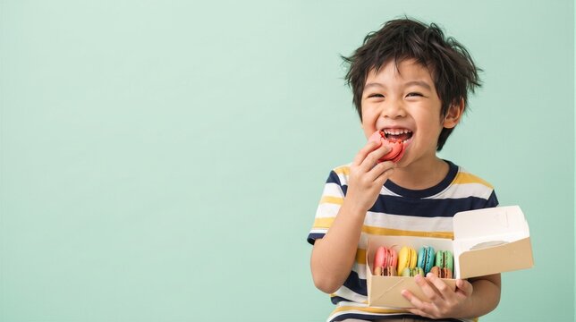 Happy young boy eating a colorful macaron from a box