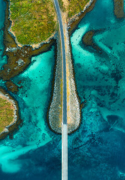 Fredvang bridges road over turquoise ocean water in Lofoten, Norway. Aerial top down drone view of coastal highway, island coast, clear sea bottom, rocks and scenic landscape in autumn