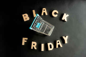 The words BLACK FRIDAY in wooden letters with a miniature shopping cart on a dark background a conceptual image of the shopping sale and seasonal discounts. © Oksana