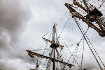Low angle view of wooden masts and intricate rigging of a historic tall ship under a dramatic cloudy sky © LidiaMara