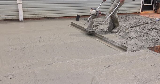 Worker uses trowel machine to smooth out wet concrete at construction site
