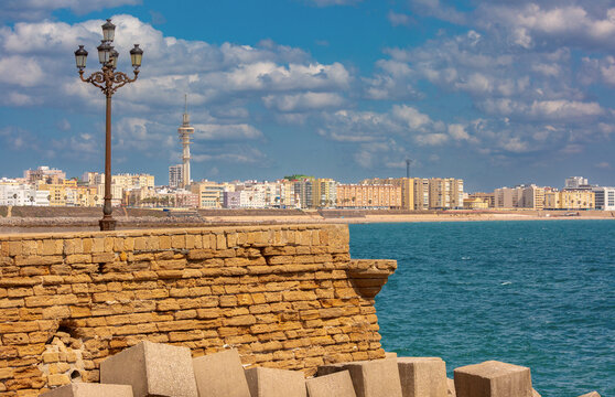 Historic coastal masonry overlooks the Atlantic Ocean with sandy beach and urban waterfront of Cadiz, Spain in the background.