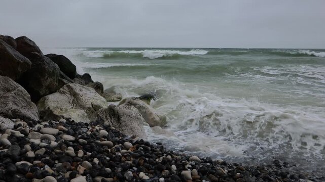Waves washing over a pebble beach at Cap Blanc-Nez, France. Panning shot of foaming surf breaking on chalk boulders and shingle on the Opal Coast under a grey overcast sky