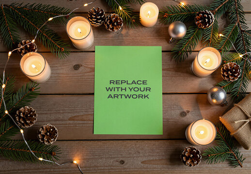 Vertical poster mockup on a wooden table with Christmas decorations, candles, pine branches, pinecones, and string lights, holiday design presentation space for artwork, festive seasonal scene