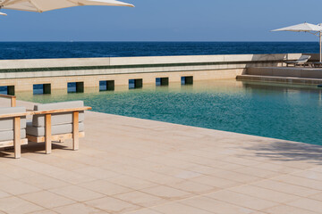 Fototapeta premium Luxury outdoor swimming pool deck with comfortable lounge chairs and white umbrellas overlooking the blue sea on a sunny day.