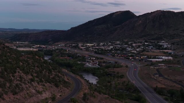 Aerial of Durango Colorado mountain town in valley at dusk with city lights and major highway US 160