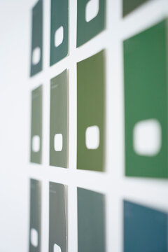 Green and blue paint color samples are arranged on a white wall for comparison