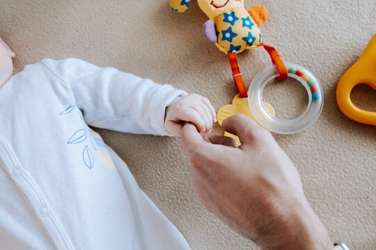  Softly cupped infant toes within caring adult palms. Delicate baby hand cradled tenderly bycexperienced adult hands in soft lighting. Gentle parental contact creates safe haven. 