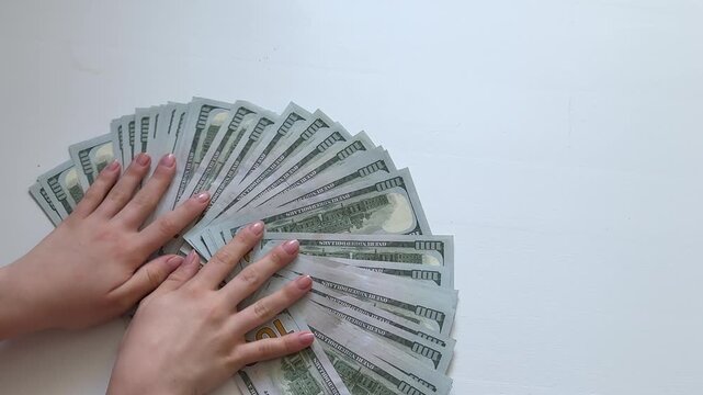 Female hands carefully spread 100 dollar banknotes into a wide semicircle on a white surface. A clean visual concept of wealth, prosperity, savings, finance, banking and cash abundance.