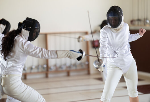 Man and woman in fencing kit engage in friendly sparring match, focusing on footwork and blade control