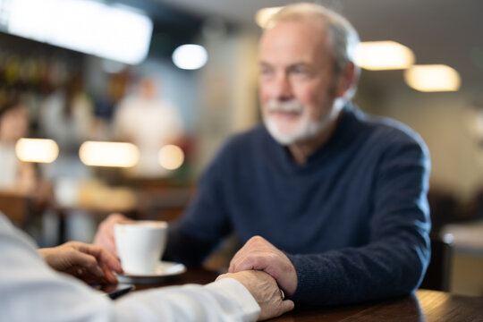 Senior man holds the hand of an elderly woman sitting at a table in a bright coffee shop, they are on a date and talking about joint plans