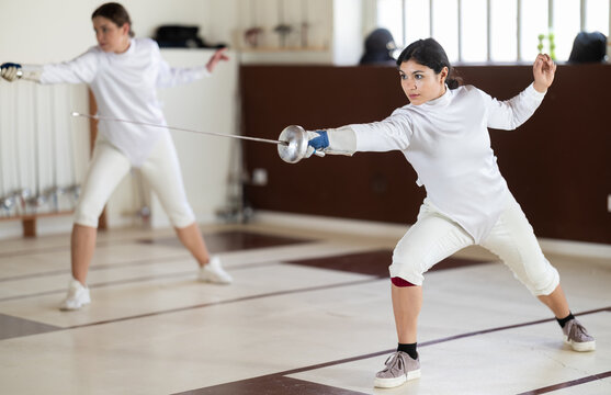 Men and women in white uniforms practice fencing techniques with foils in their hands