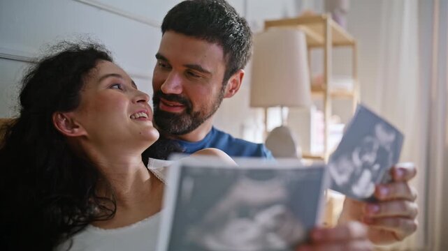 Expecting couple looking sonogram scan photos. Pregnant wife husband embracing