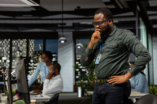 Black businessman reflects on a problem in the office after hours using methodical planning and critical thinking to reach a decision that balances rationality with innovation in a business setting.