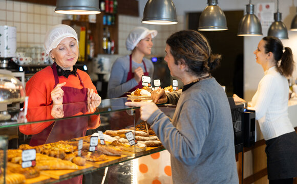 senior female bakery assistant consults customer, tells about availability of gluten-free, lactose-free and meat-free baked goods. Products for people with food intolerances and allergies