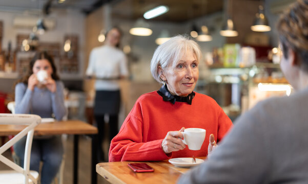 Elderly woman meets a man in a cafe. Conversation over a cup of coffee