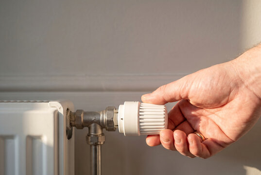 Hand adjusting a white thermostatic radiator valve attached to a modern, clean white panel radiator