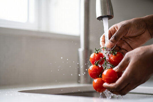 The hands of a woman washing fresh, bright red vine tomatoes under a stream of clear running water