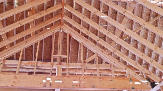 Completing roof framing in frame building under construction wooden beams are positioned above.