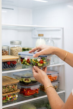 Person's hands placing a clear glass food container filled with fresh salad onto a middle shelf