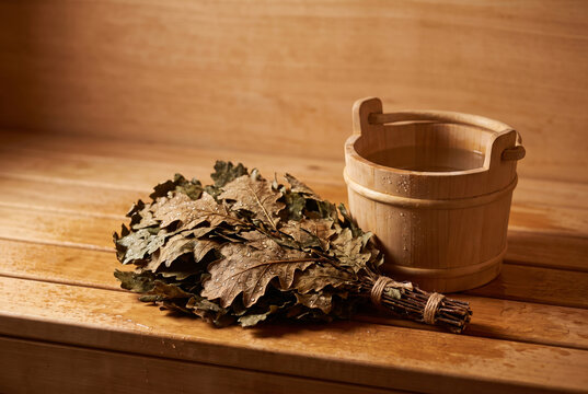 Traditional dried oak leaf bath broom (venik) resting beside a wooden water bucket