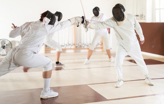 Fencers practice epee techniques during an intense workout in the gym. Group fencing training