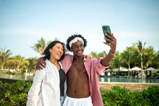 Trendy digital creator couple taking selfie by the beach, sharing travel content for social media