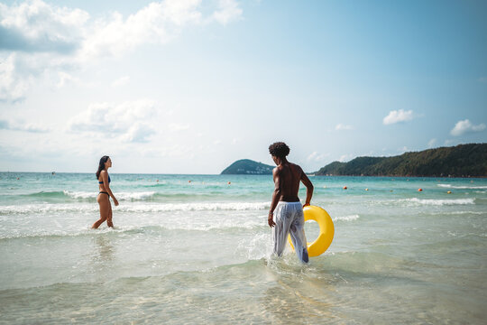 Friends, diverse couple having fun with colorful inflatable rings at the seaside