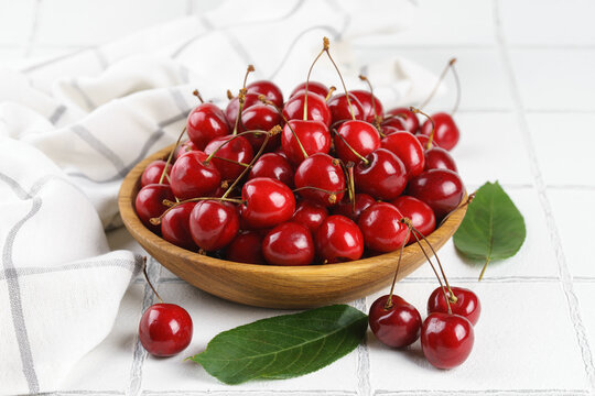 Fresh ripe red sweet cherries in wooden bowl with green leaves on light textured background. Healthy organic summer fruit, juicy red berries, natural freshness, healthy eating, seasonal food